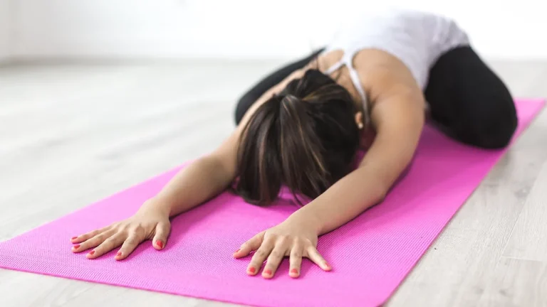Une femme en posture de l'enfant sur un tapis de yoga rose