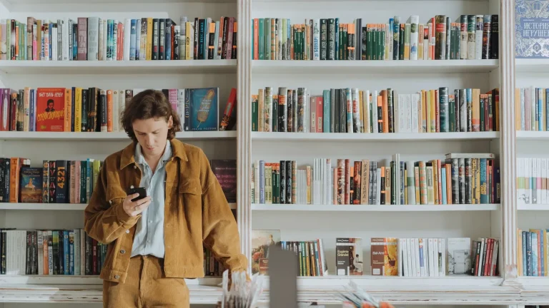 Un jeune consulte son smartphone au milieu des rayonnages d'une librairie