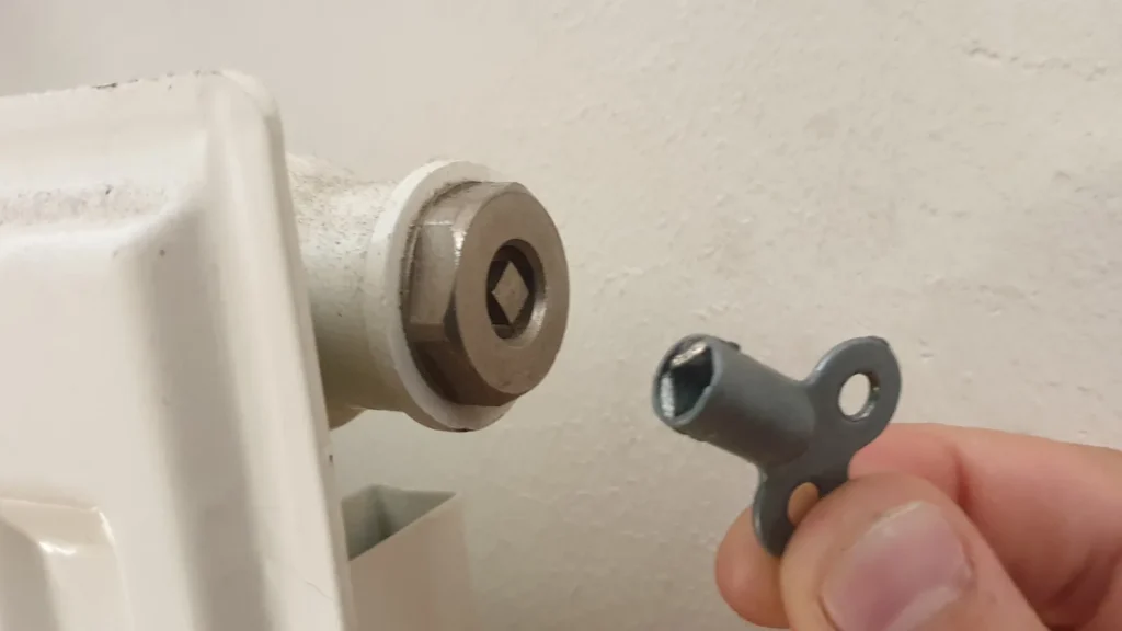 Une main tient une clé de purge devant la vis d'un radiateur