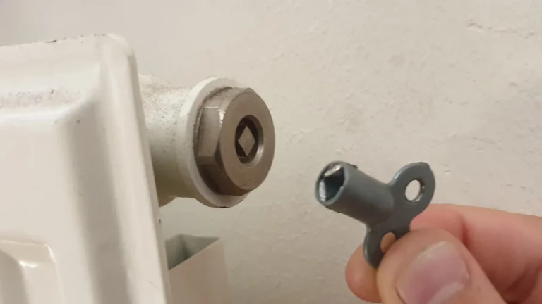 Une main tient une clé de purge devant la vis d'un radiateur