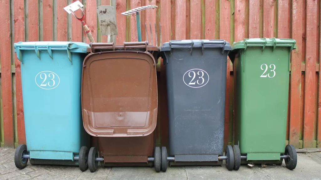 Des bacs à déchets roulants alignés devant une palissade en bois